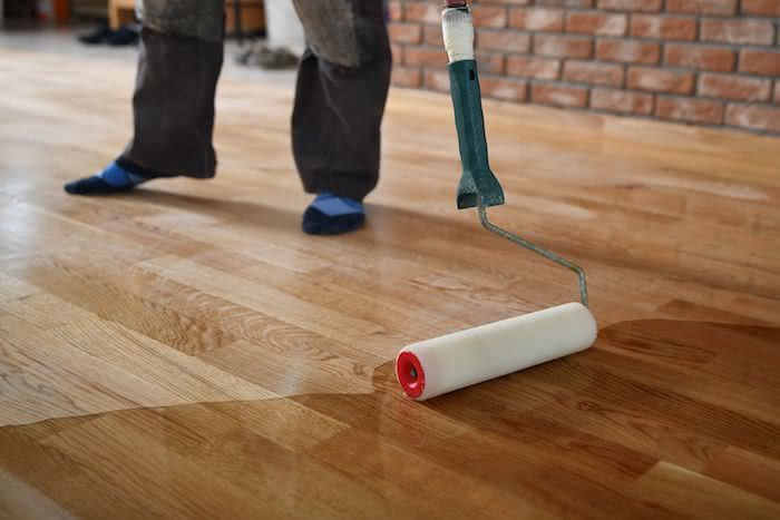Profissional aplicando verniz em piso de madeira