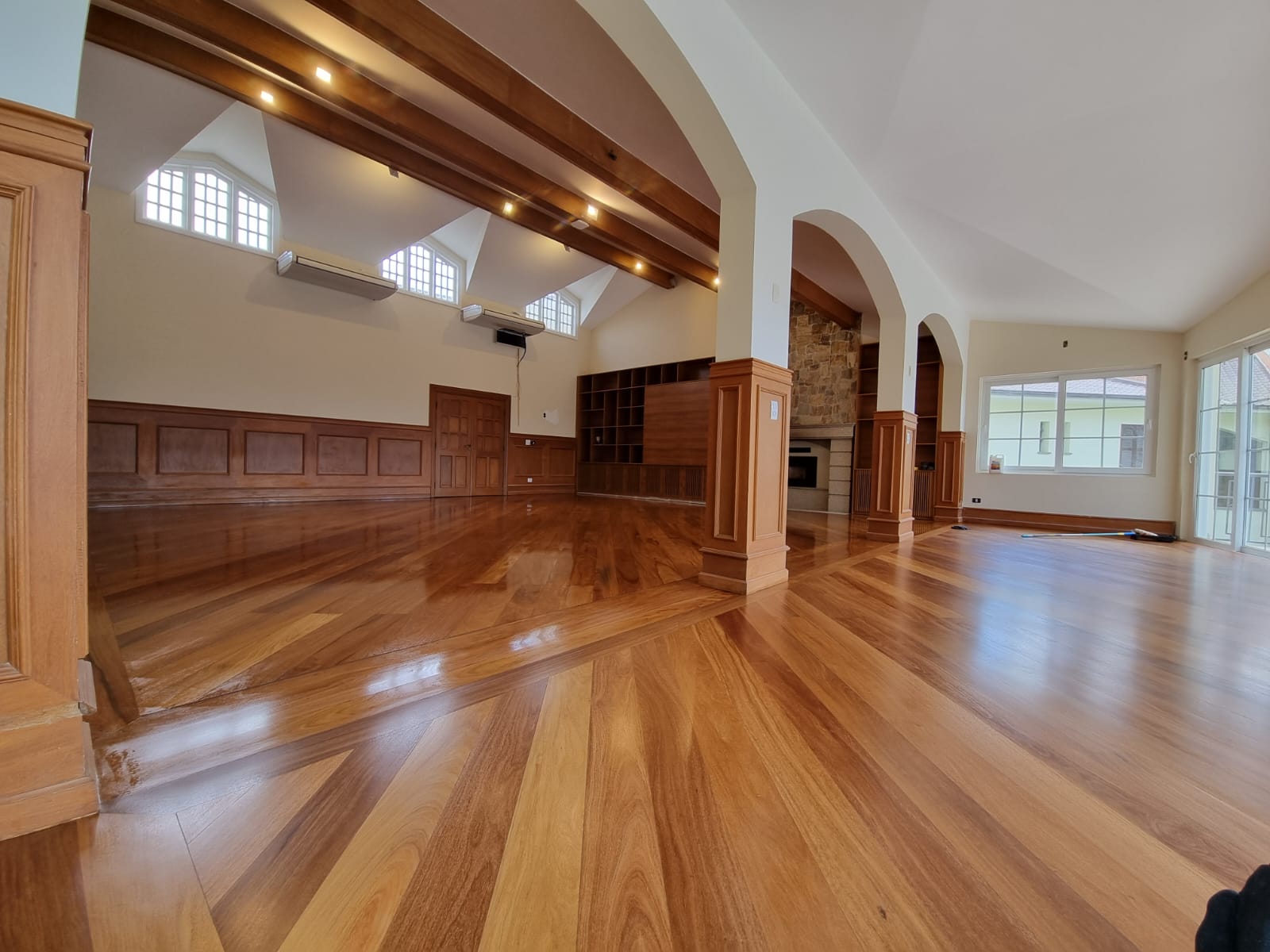 Salão amplo com piso de madeira restaurado e arcos